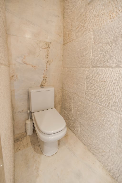 Aseo con paredes de piedra caliza texturizada y mármol pulido, creando un ambiente orgánico y elegante con materiales naturales.