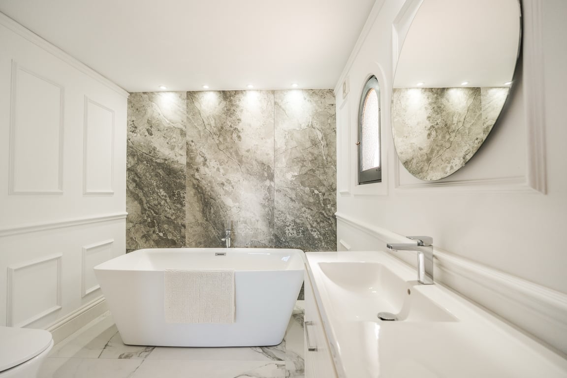 Baño elegante con bañera exenta, pared de mármol con iluminación integrada y molduras clásicas que aportan un diseño atemporal.