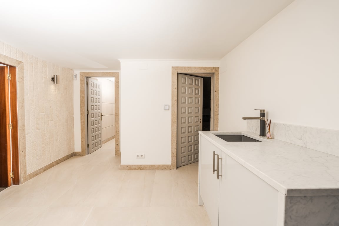 Distribuidor con mueble auxiliar de mármol y fregadero. Cuenta con marcos de puertas en piedra tosca y suelos cerámicos claros en un ambiente minimalista.