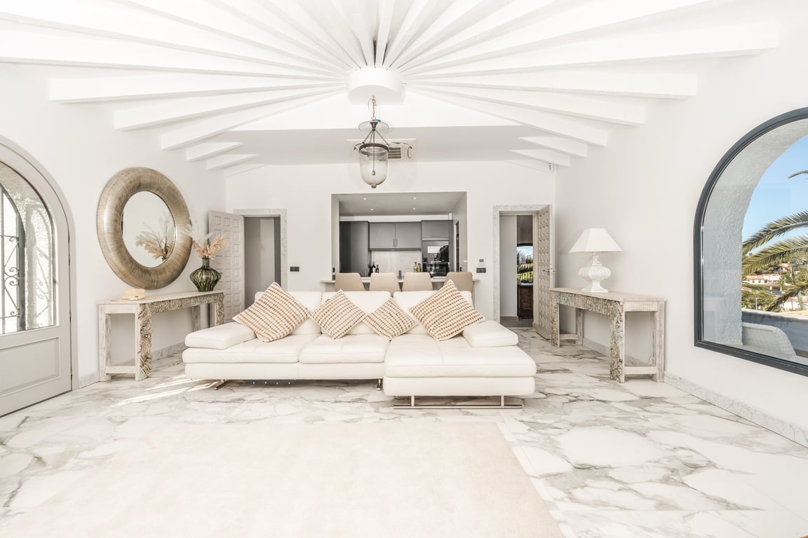 Salón circular con techos de vigas radiales blancas, suelo de mármol veteado y grandes ventanales en arco que ofrecen abundante luz natural y vistas al entorno.