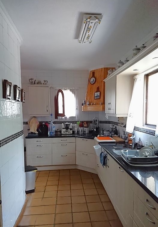 Cocina independiente equipada con armarios blancos, encimeras oscuras y suelos de gres. Incluye una campana con revestimiento de madera y entrada de luz natural.