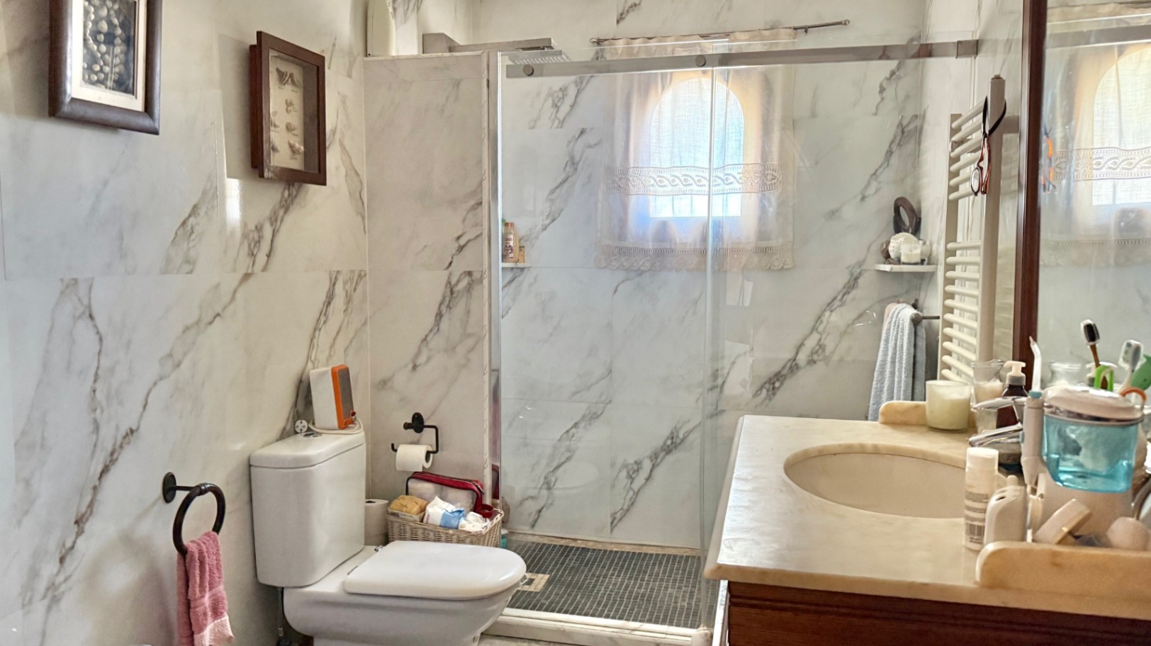 Cuarto de baño con paredes revestidas de mármol, ducha de obra con mampara de cristal y lavabo con encimera de piedra natural.