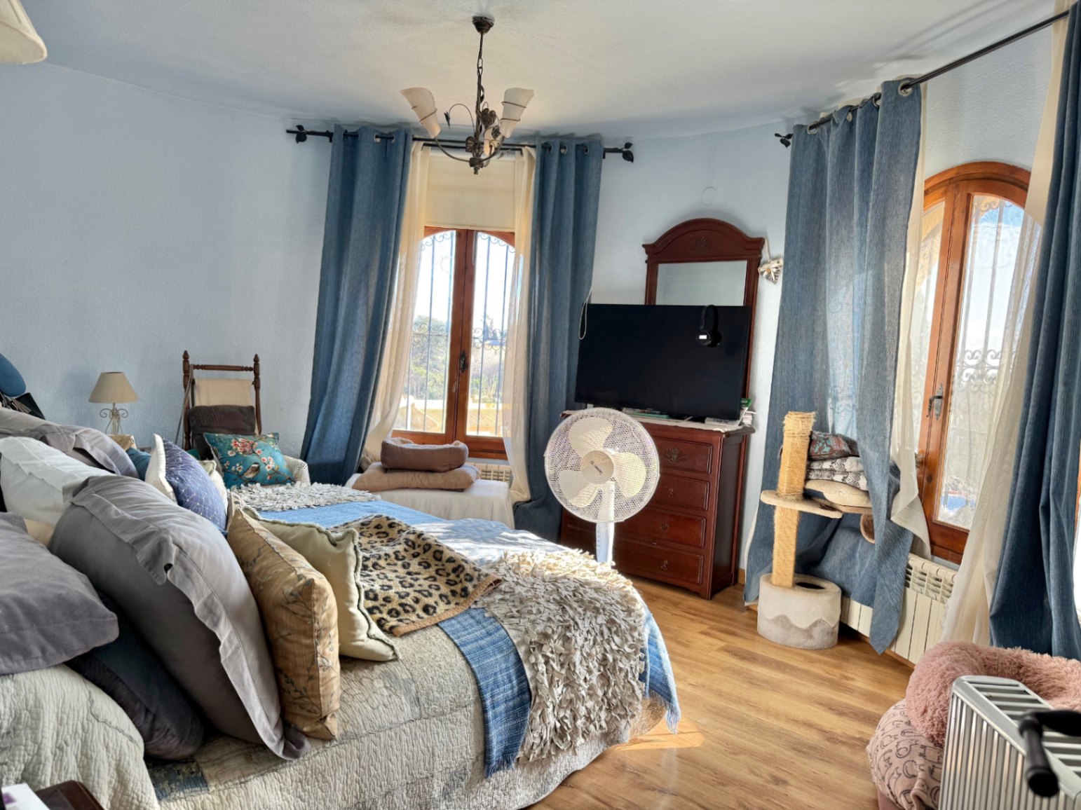Dormitorio con pared curva, suelo de tarima y ventanas de madera con rejas. Incluye mobiliario clásico de madera, radiador y abundante luz natural.