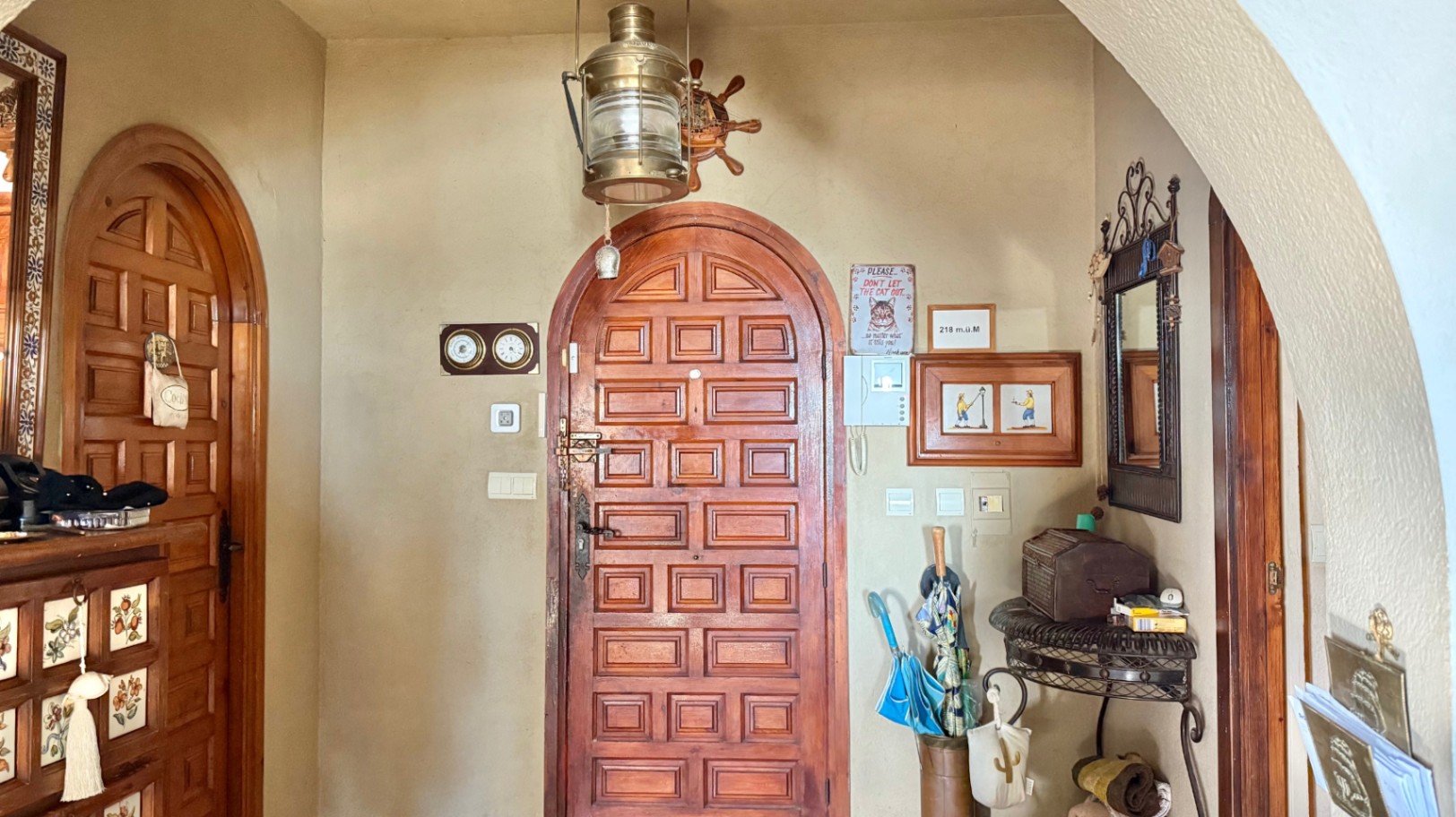 Hall de entrada con puertas de madera maciza en arco, decoración de temática náutica con lámpara de latón y mobiliario de hierro forjado bajo un arco estructural.