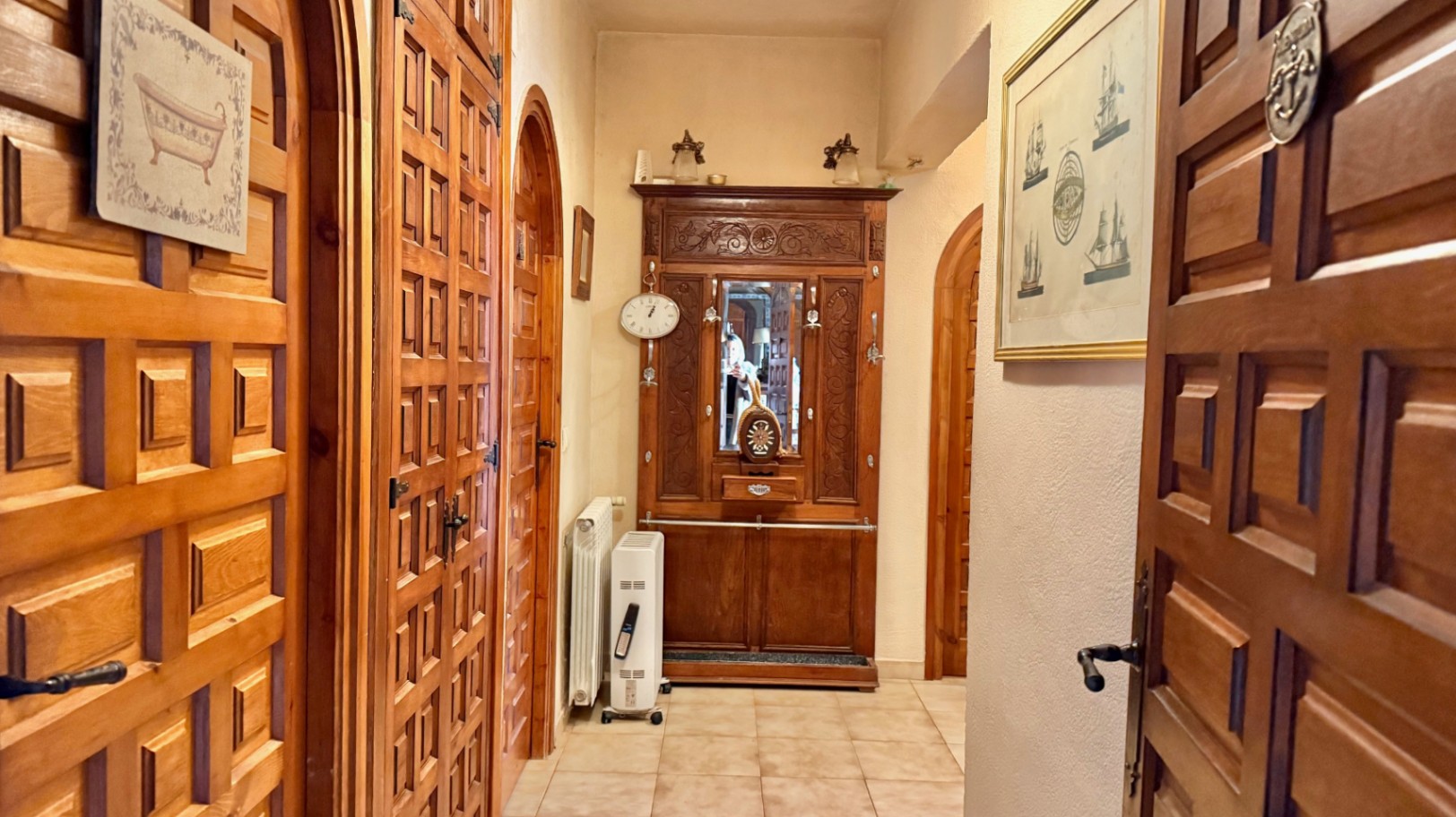 Pasillo distribuidor con puertas de madera maciza de estilo castellano y marcos en arco. Incluye un mueble de entrada tallado y suelos de baldosa cerámica clara.
