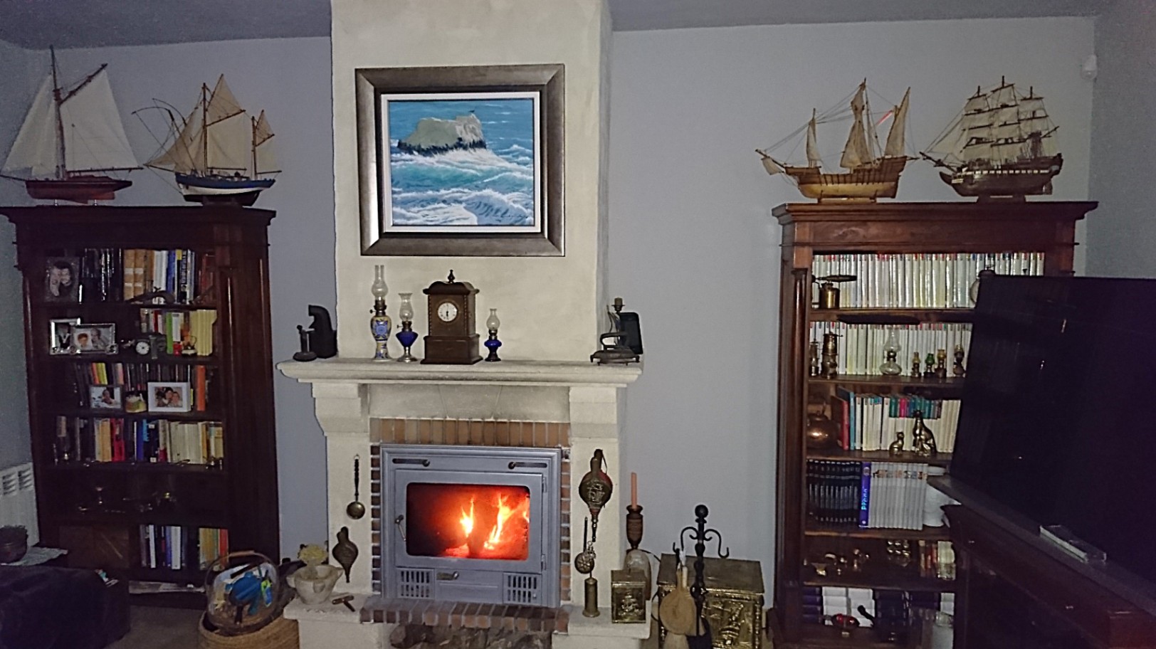 Salón tradicional con chimenea de obra integrada, flanqueada por librerías de madera clásica y decorada con maquetas navales y cuadros de temática marina.