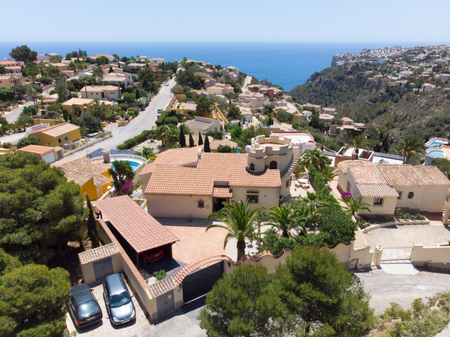 Vista aérea de la villa destacando su torre característica, el porche para vehículos y la parcela ajardinada con vistas panorámicas al mar Mediterráneo.