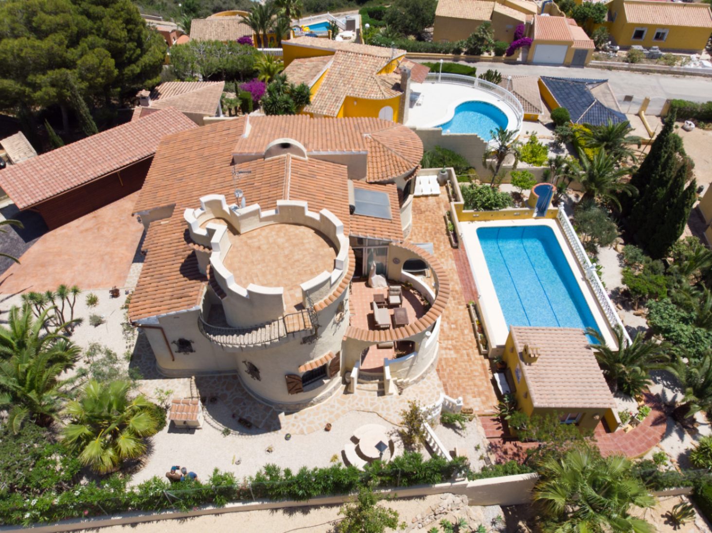 Vista aérea de la villa destacando su torre circular con terraza almenada, piscina rectangular y amplias zonas de terraza pavimentadas rodeadas de vegetación mediterránea.