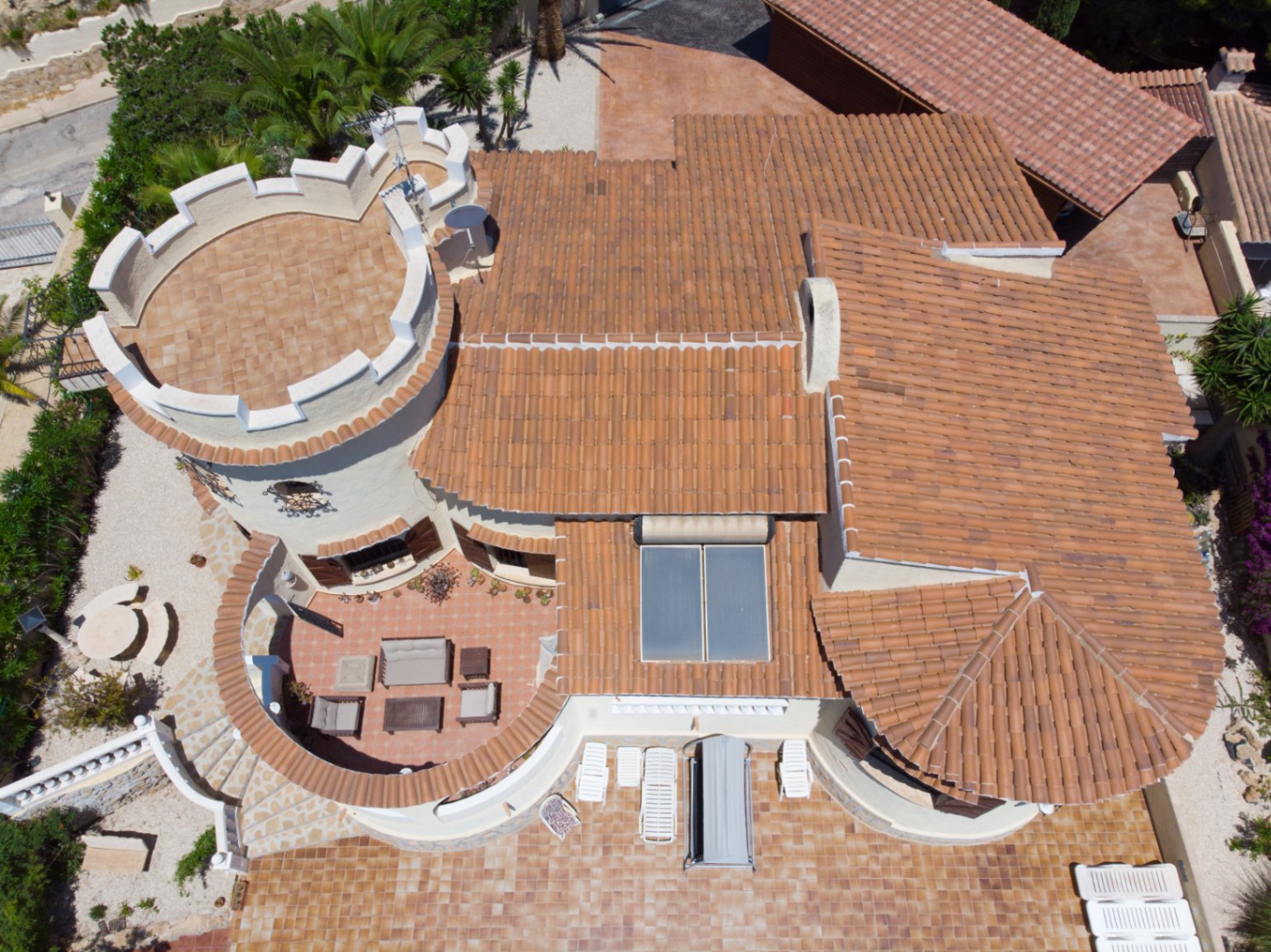 Vista aérea de la villa destacando su torreón almenado, los tejados de teja cerámica con paneles solares y las amplias terrazas exteriores amuebladas.
