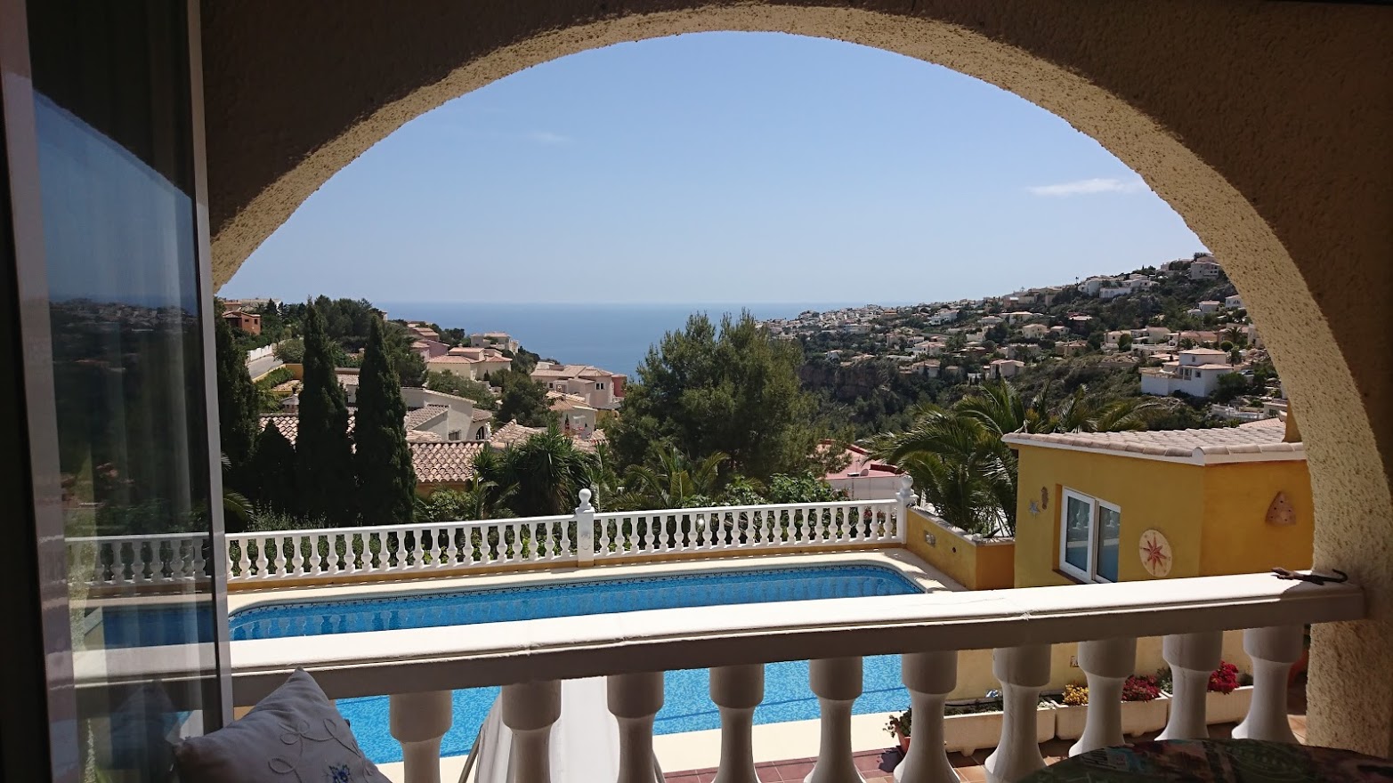 Vista panorámica al mar Mediterráneo enmarcada por un arco tradicional, con la piscina privada y la costa de Benitachell en primer plano.
