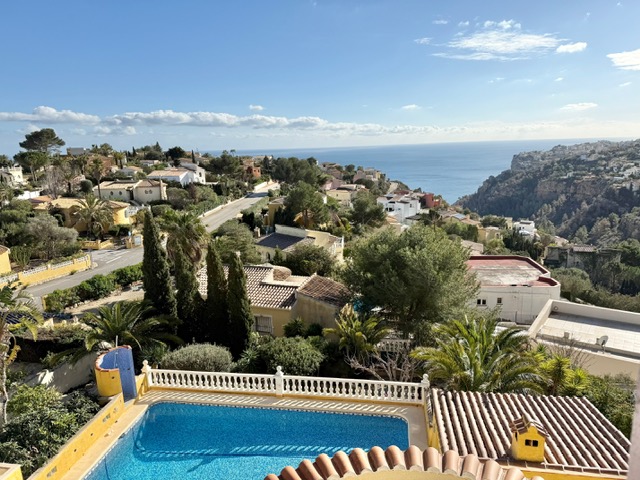 Vista panorámica desde la propiedad que muestra la piscina rectangular, el jardín mediterráneo y las vistas despejadas al mar y los acantilados de Benitachell.