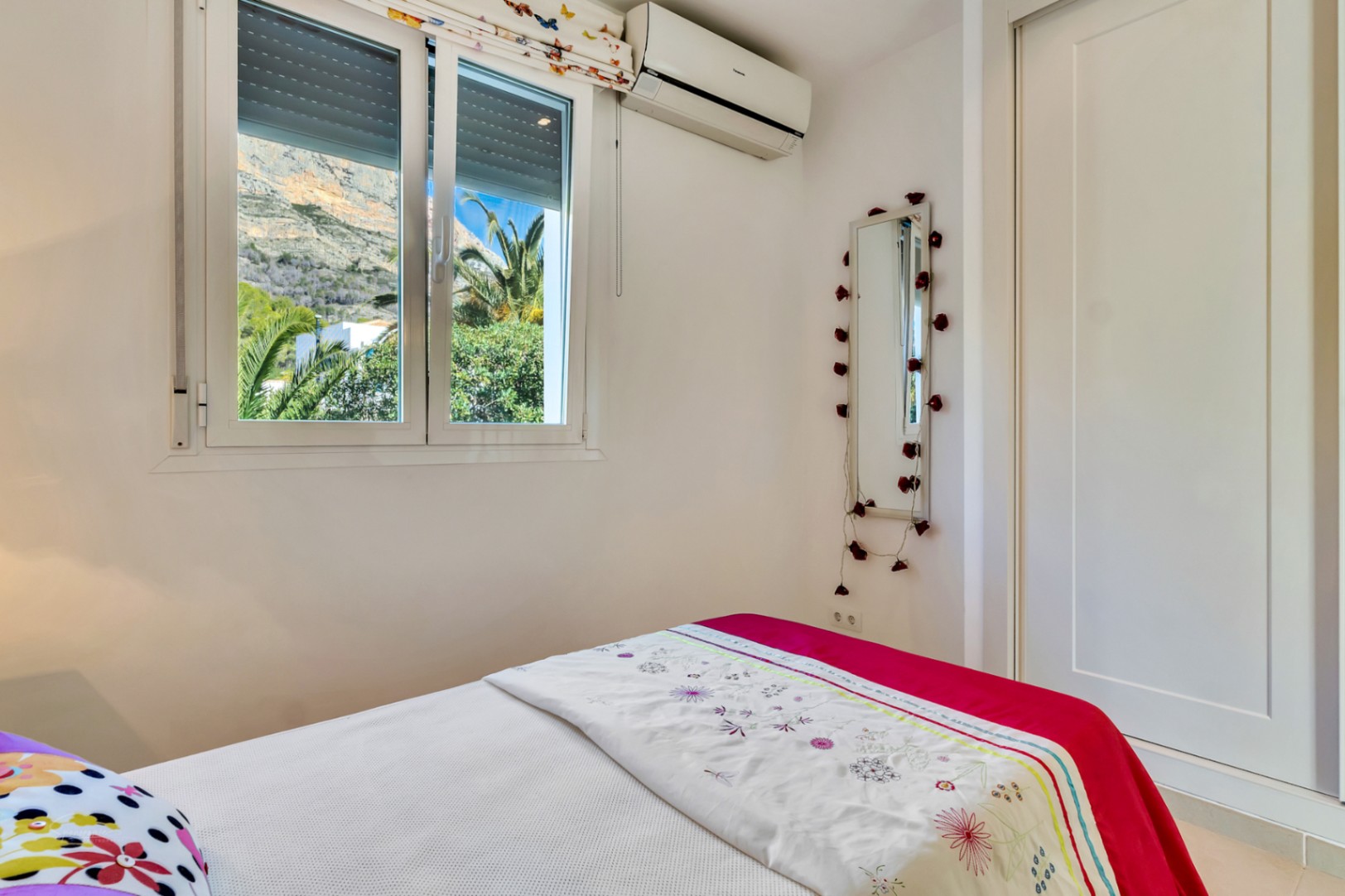 Dormitorio luminoso con aire acondicionado, armario empotrado blanco y ventana con vistas directas a la montaña del Montgó.