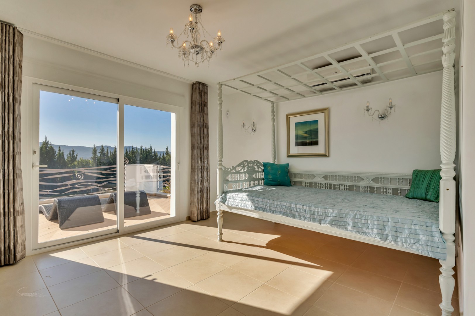 Dormitorio luminoso con una cama de dosel blanca tallada y acceso directo a una terraza privada con vistas despejadas al valle y las montañas.