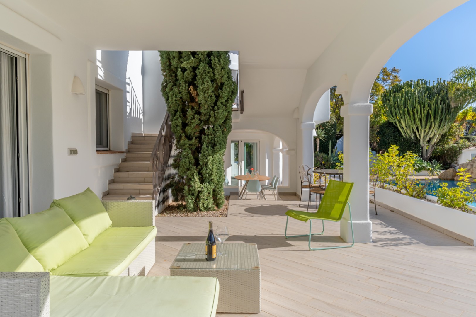 Naya cubierta con arcos blancos, mobiliario de exterior en tonos lima y vistas directas a la piscina y al jardín mediterráneo.