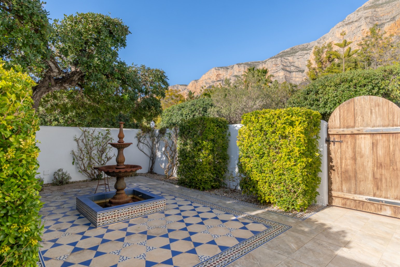 Patio de estilo andaluz con fuente ornamental de tres niveles, suelos de baldosas hidráulicas en azul y blanco, y vistas despejadas al macizo del Montgó.