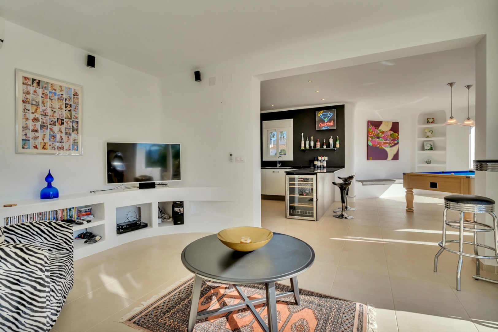 Salón de planta abierta con zona de TV, estanterías de obra curvas y un área de entretenimiento que incluye mesa de billar y bar con vinoteca integrada.