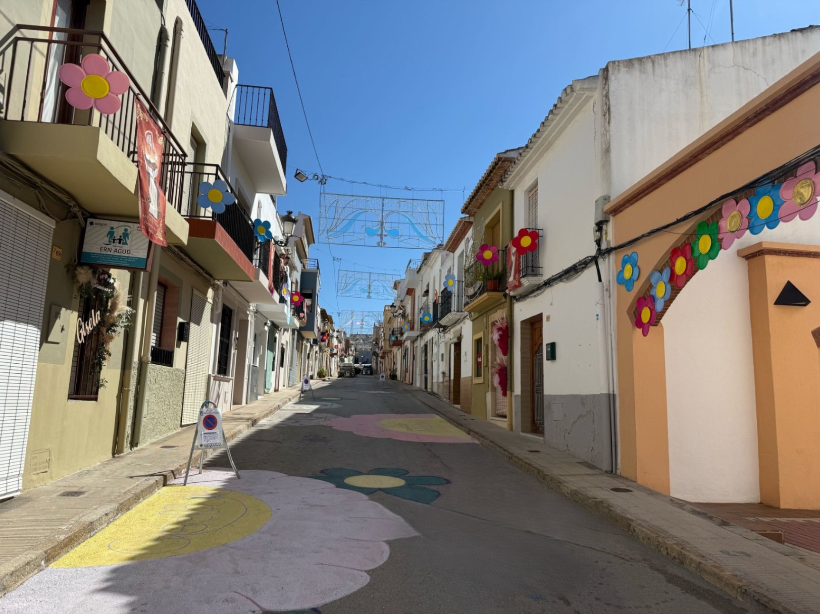 Calle de Teulada decorada con flores pintadas y adornos festivos colgantes.
