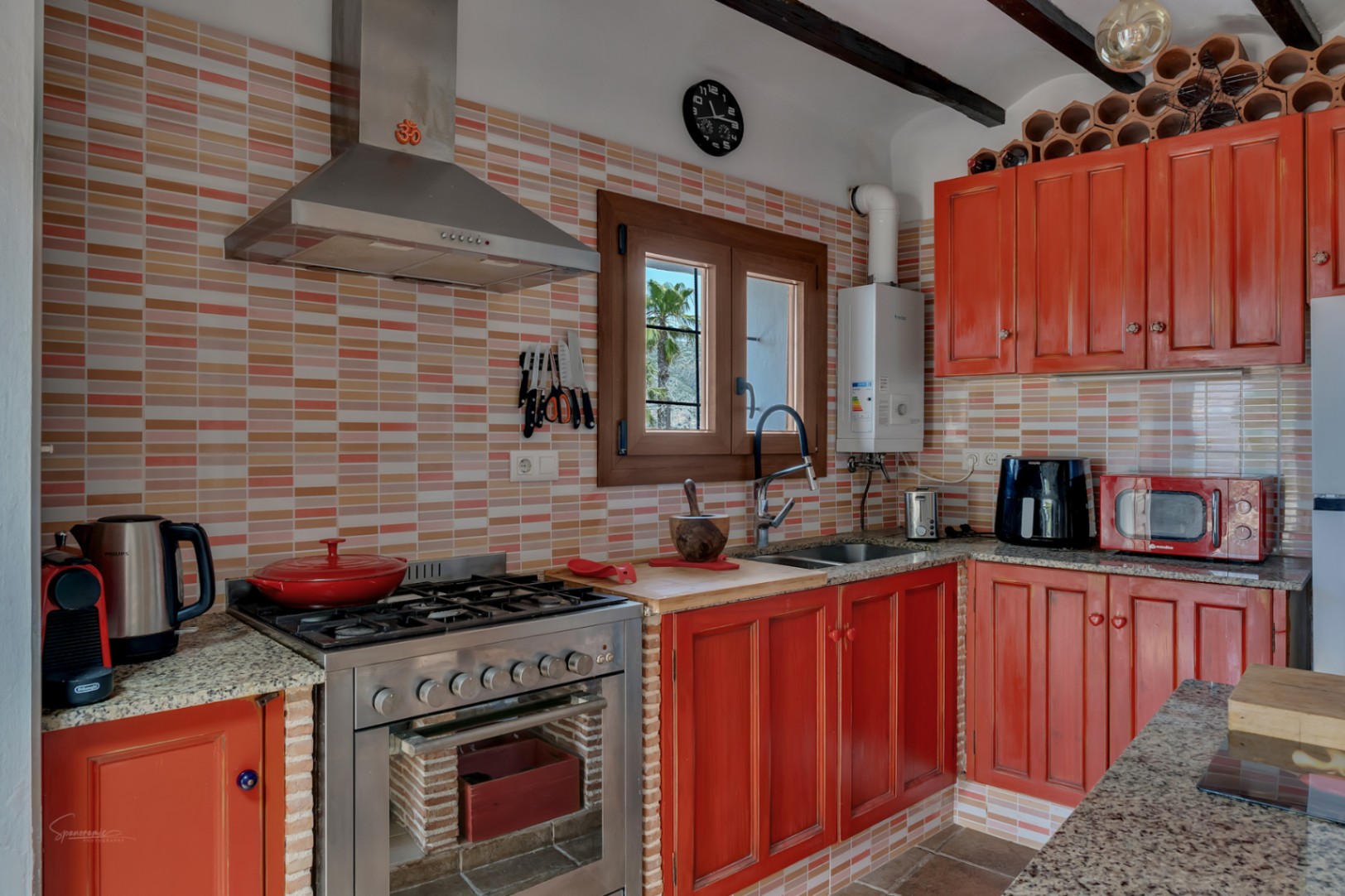 Cocina rústica con azulejos coloridos, muebles de madera rojiza y encimera de granito.
