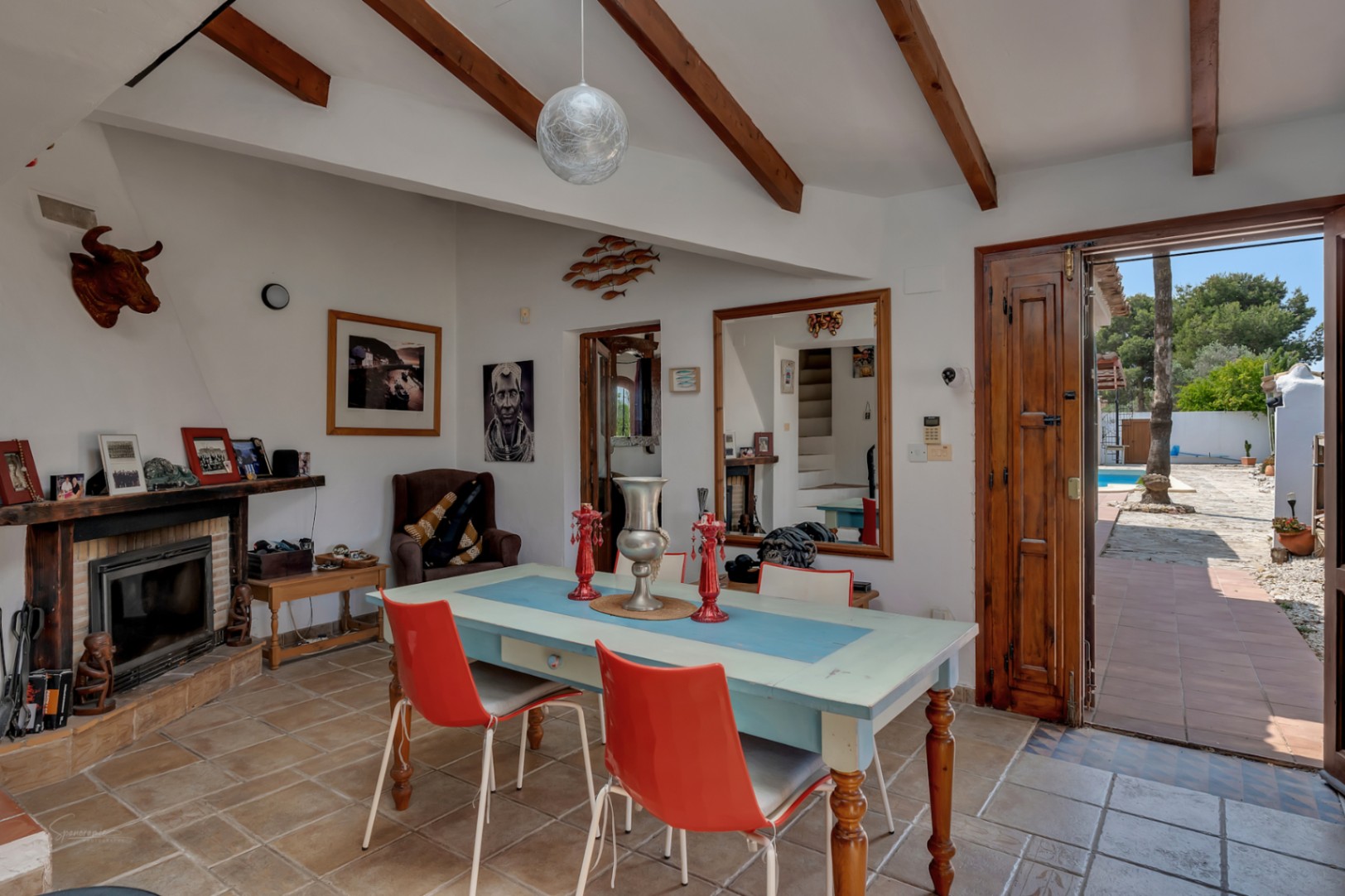 Comedor rústico con chimenea, vigas de madera y acceso al jardín con piscina en Teulada.