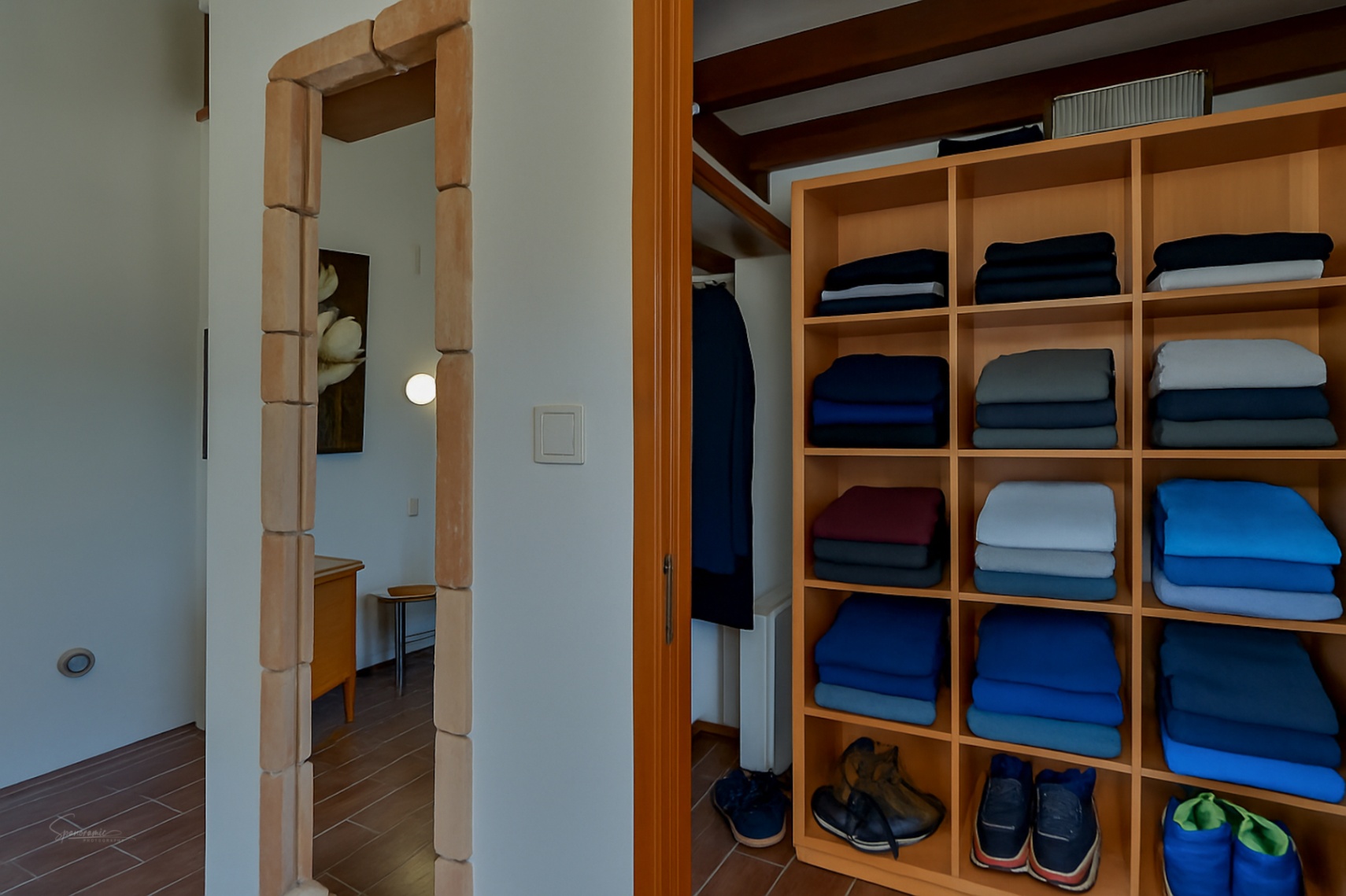 Detalle de vestidor con estanterías de madera clara y puerta con marco de piedra en Teulada.