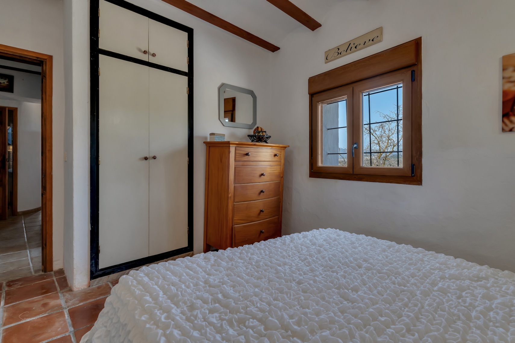 Dormitorio con armario empotrado blanco, cómoda de madera y ventana con carpintería de madera.