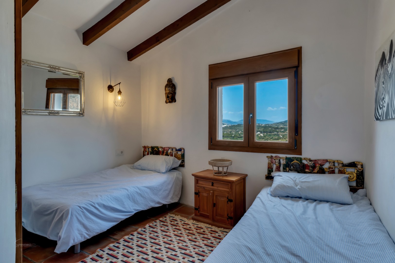 Dormitorio con dos camas individuales, vigas de madera vistas y vistas al paisaje desde la ventana.