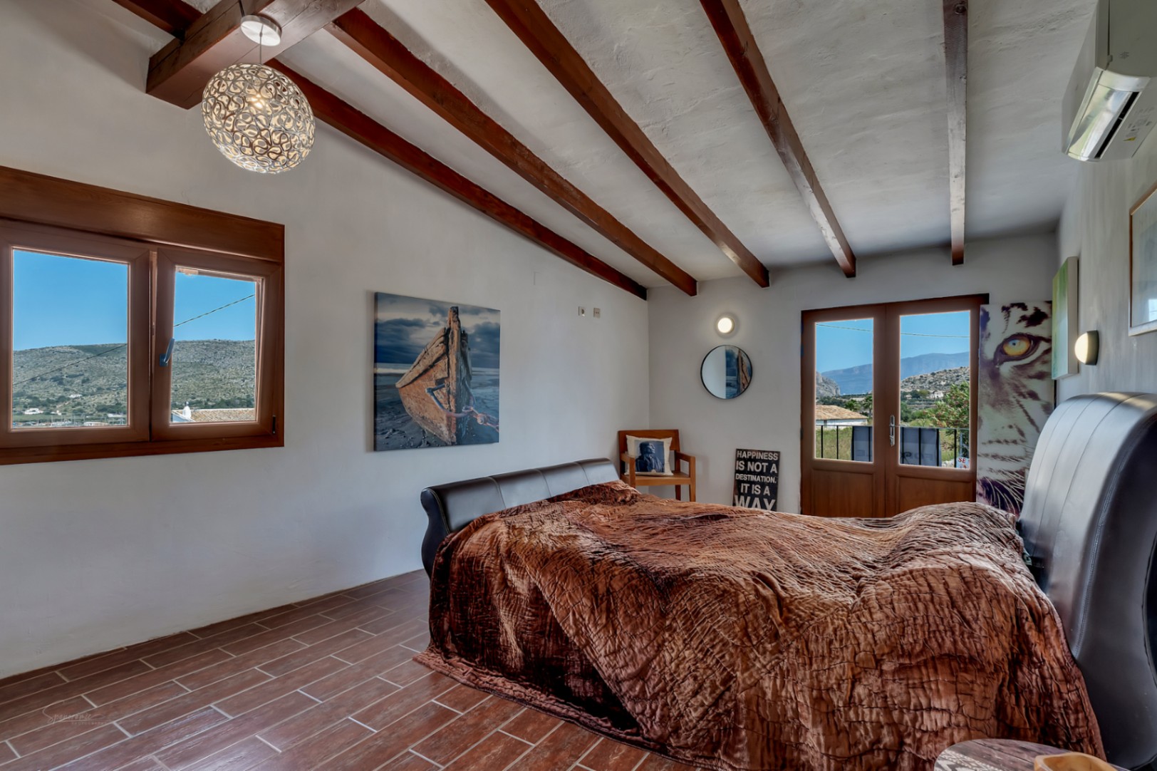 Dormitorio rústico con vigas de madera, suelo de baldosas y vistas a la montaña.