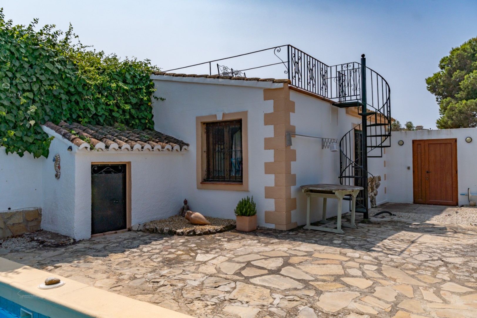 Exterior de casa de campo con escalera de caracol, anexo con puerta de hierro y suelo de piedra.