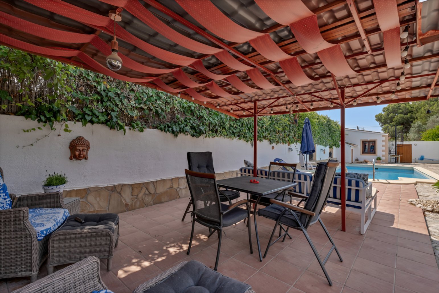 Terraza cubierta con toldo rojo y suelo de baldosas. Pared blanca con decoración de Buda y jardín vertical.