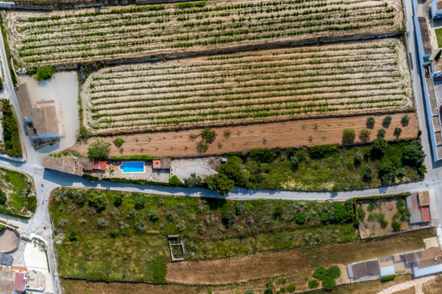 Vista aérea de finca rústica con piscina en Teulada, rodeada de campos de cultivo y vegetación mediterránea.