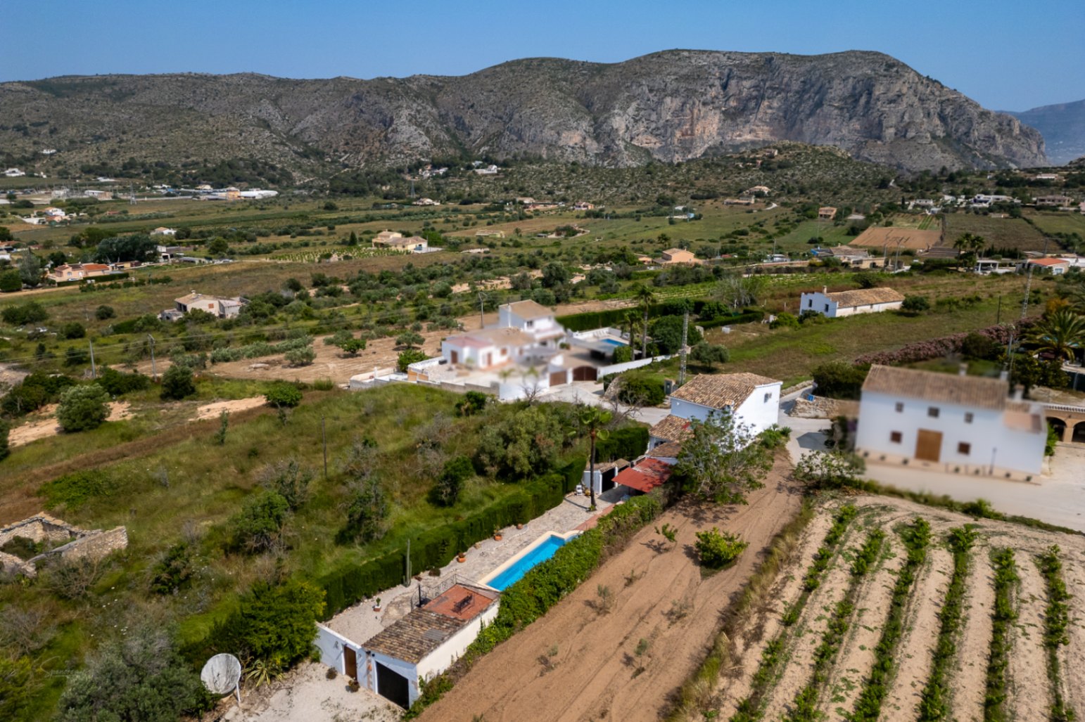 Vista aérea de la finca en Teulada con piscina alargada, jardín maduro y vistas a la montaña.