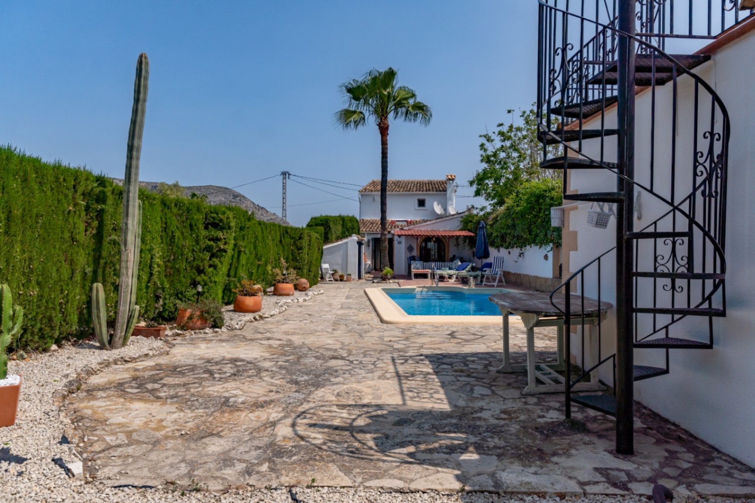 Vista del patio con piscina, escalera de caracol de hierro y seto alto en Teulada.