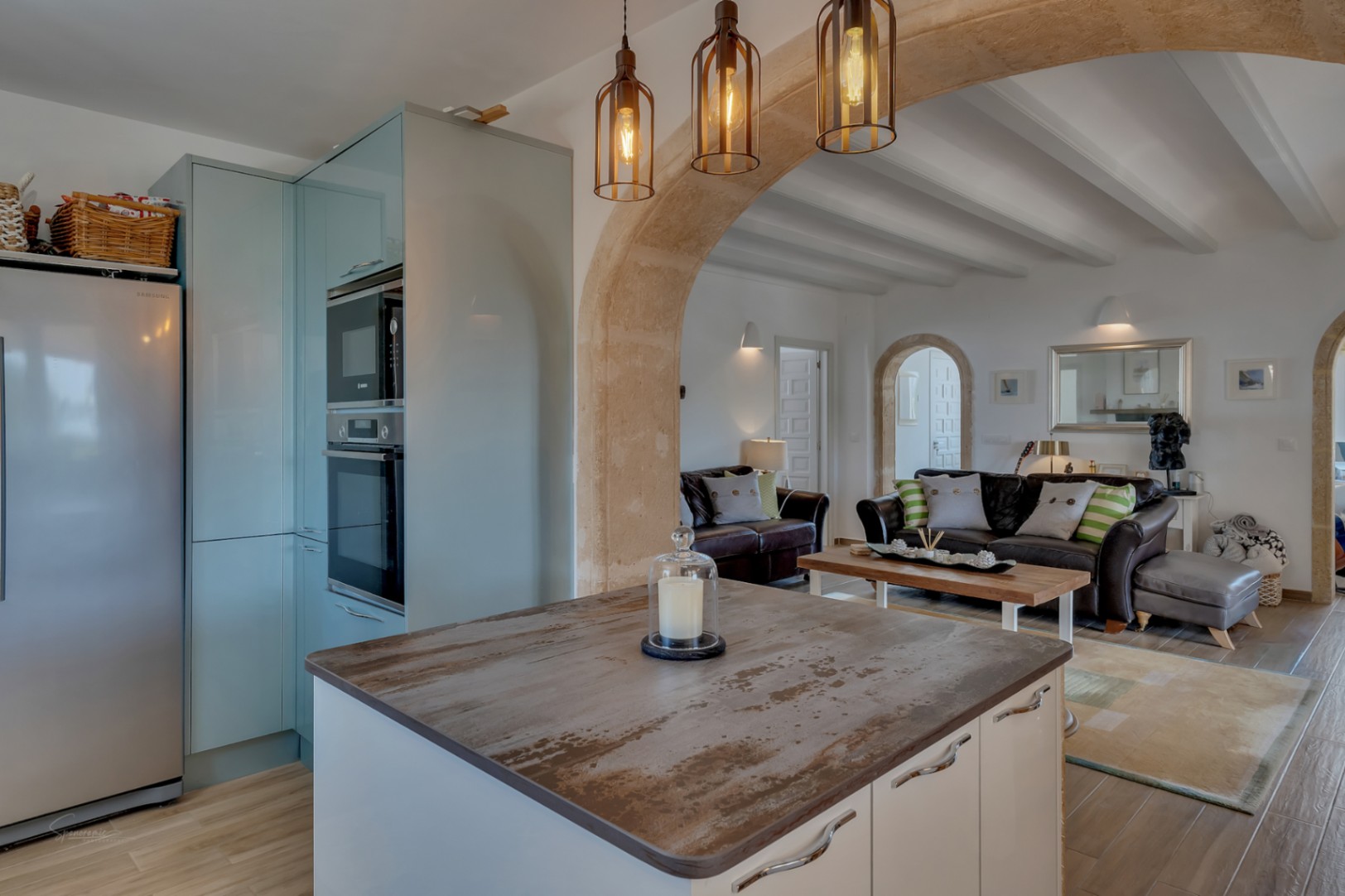 Cocina abierta con isla y salón adyacente en villa de Jávea. Diseño mediterráneo con arcos de piedra.