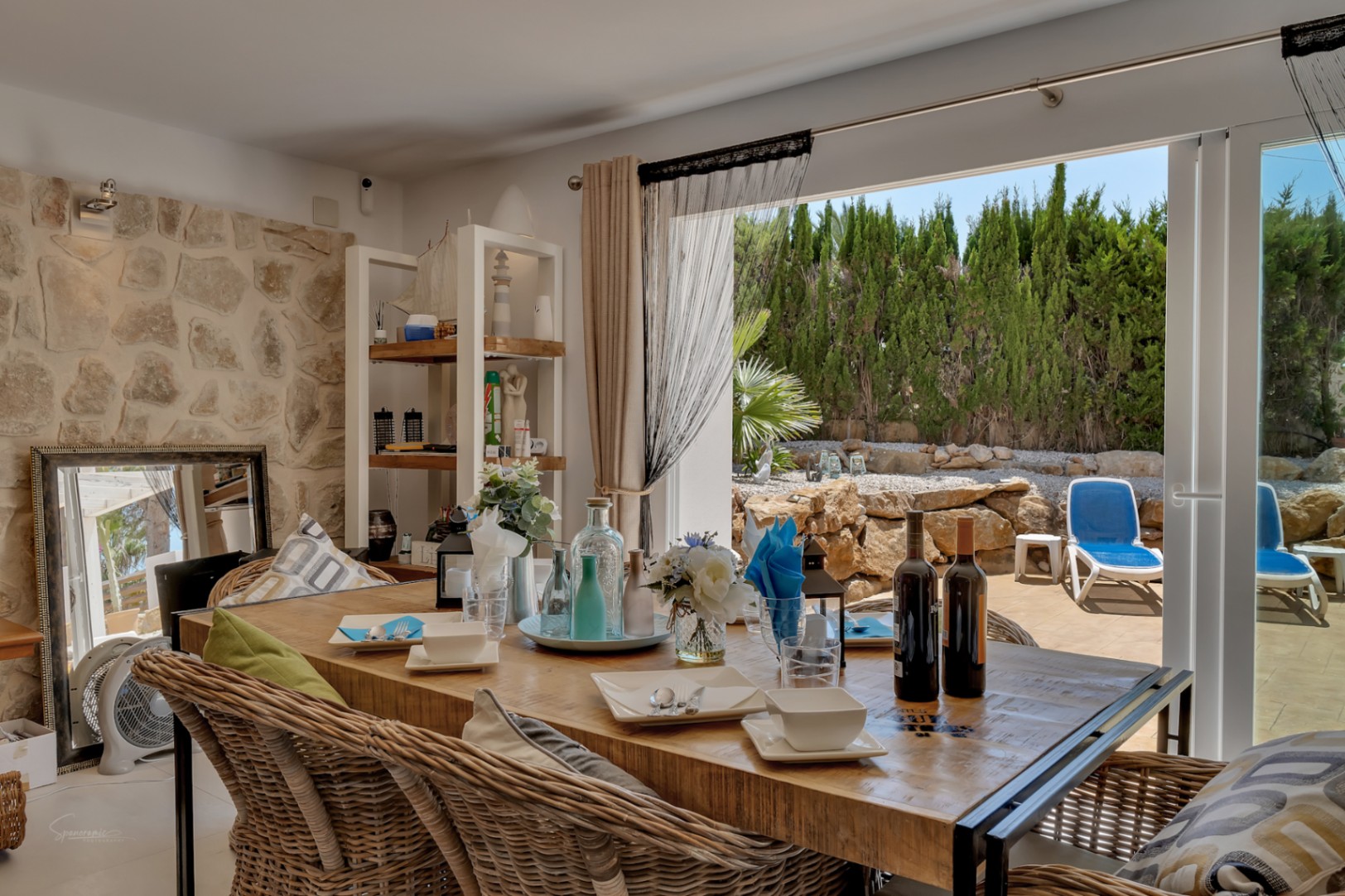 Comedor luminoso con mesa de madera y sillas de mimbre, que conecta con la terraza y el jardín.