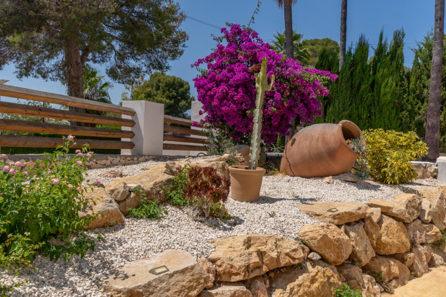 Detalle del jardín mediterráneo con cantos rodados, buganvilla y una tinaja decorativa.