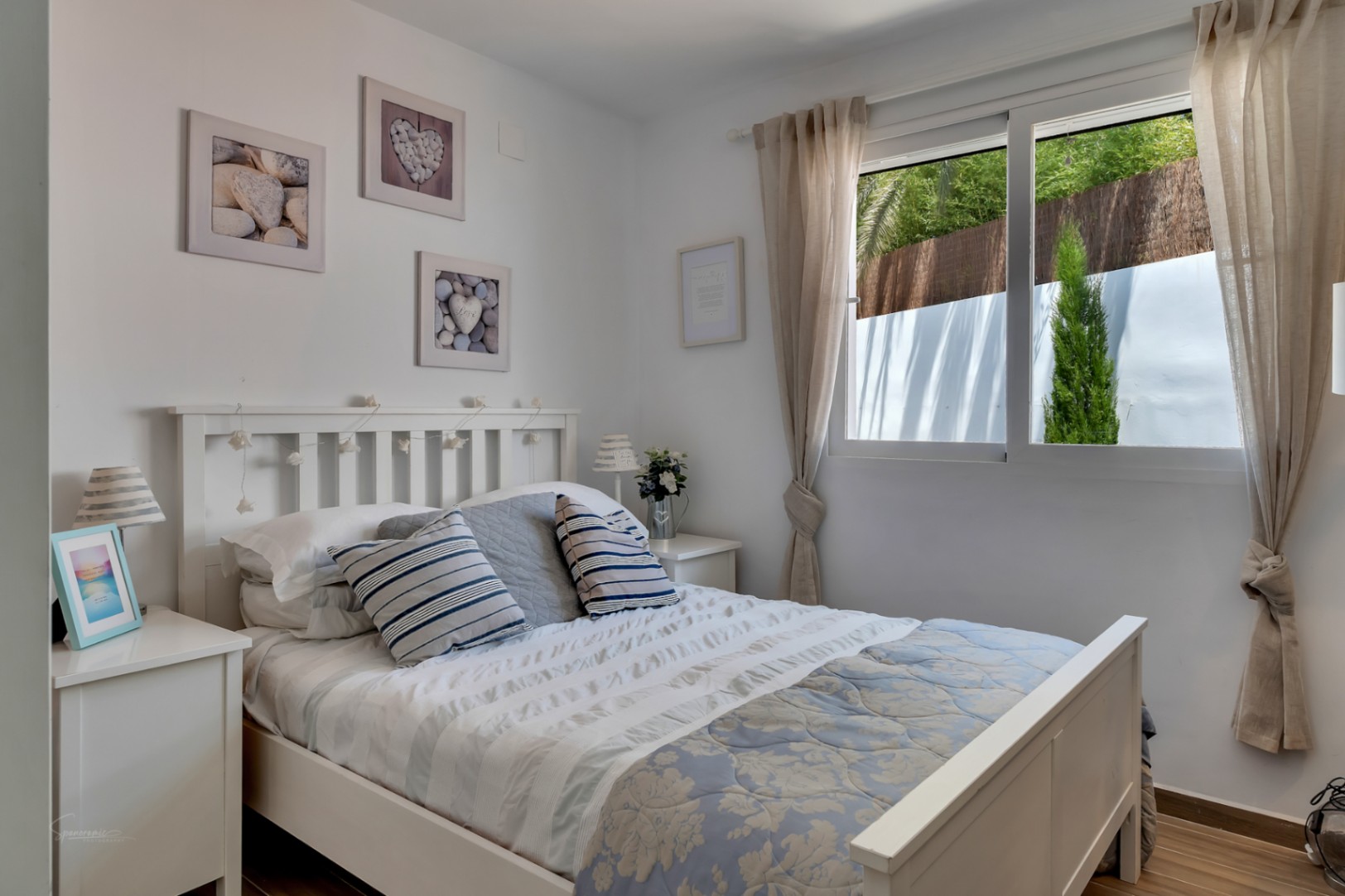 Dormitorio luminoso con cama de madera blanca, ropa de cama azul y decoración temática de playa.