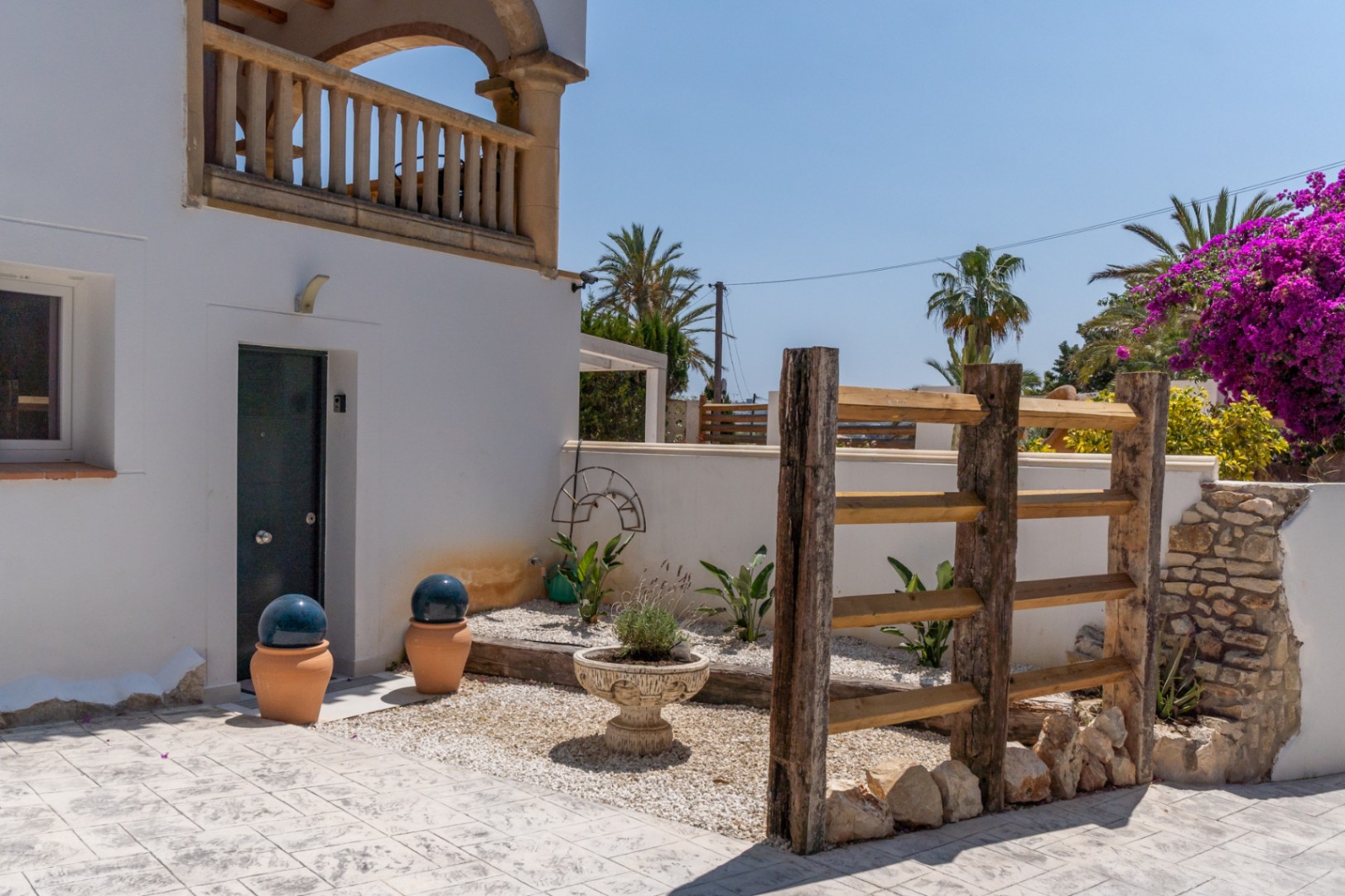 Entrada lateral con jardineras de cerámica y estructura rústica de madera.
