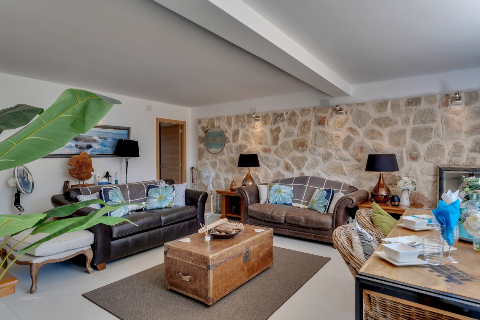 Salón con pared de piedra rústica, sofás de cuero marrón y un baúl antiguo como mesa de centro.