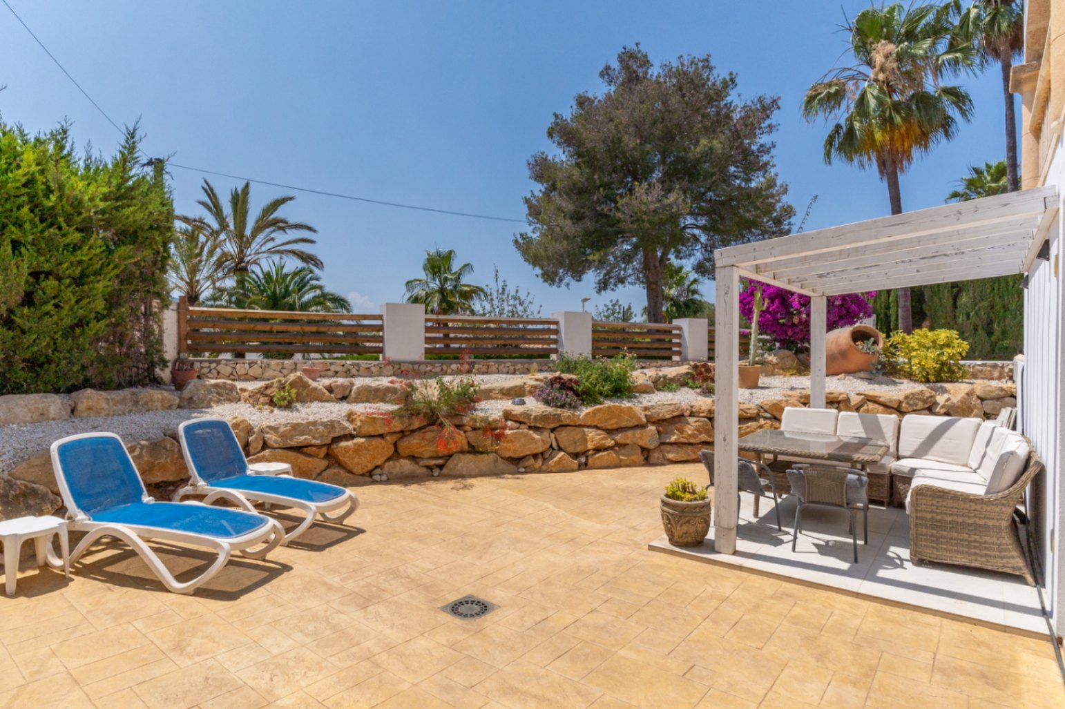 Terraza con tumbonas azules y cenador con muebles de exterior en Jávea.