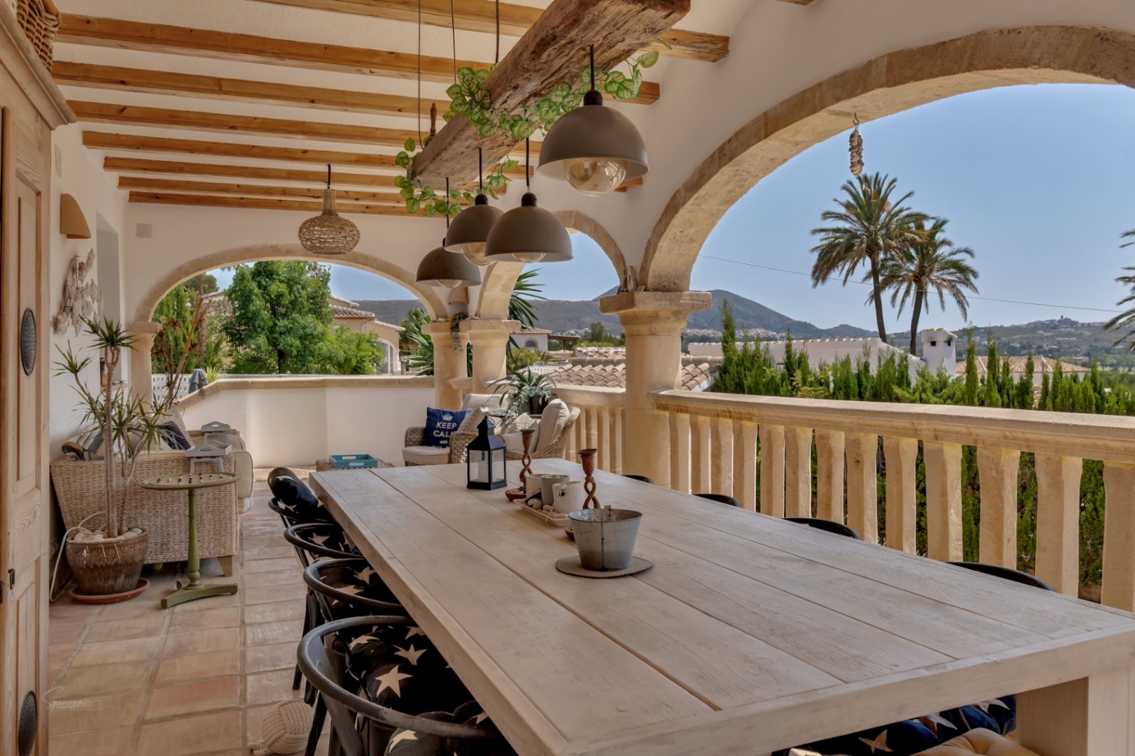 Terraza cubierta con arcos de piedra y mesa de comedor de madera clara con vistas a la montaña.