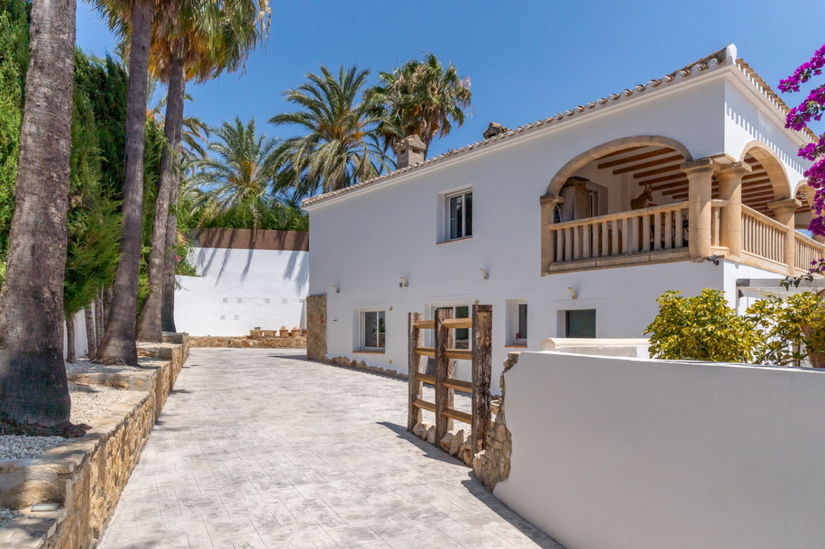 Vista exterior de la villa en Jávea, con entrada de piedra y fachada blanca. Balcón con arcos y columnas.