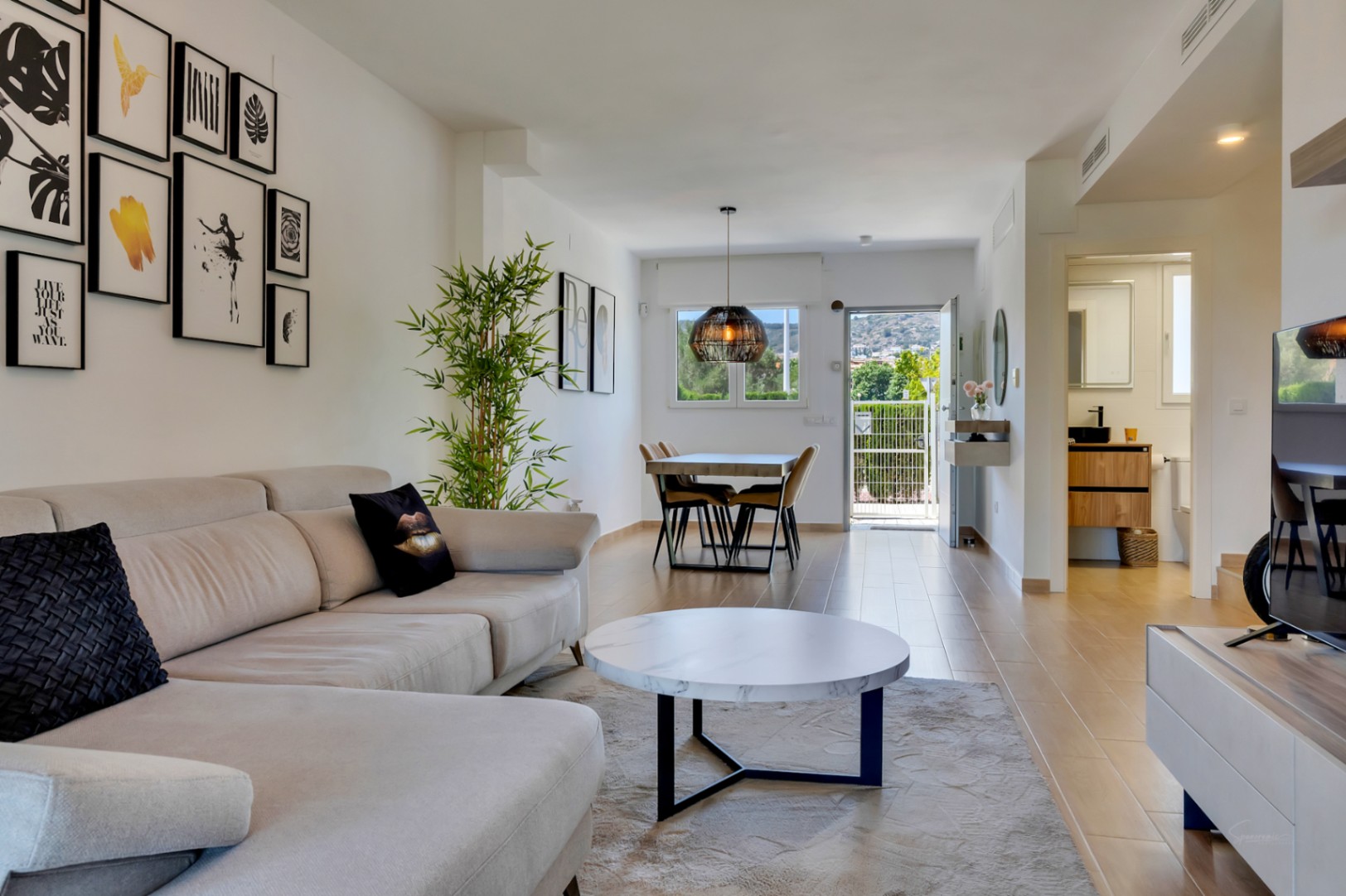Amplio salón comedor de concepto abierto con suelos cerámicos, sofá rinconero y una moderna decoración de pared que conecta con el área de comedor.