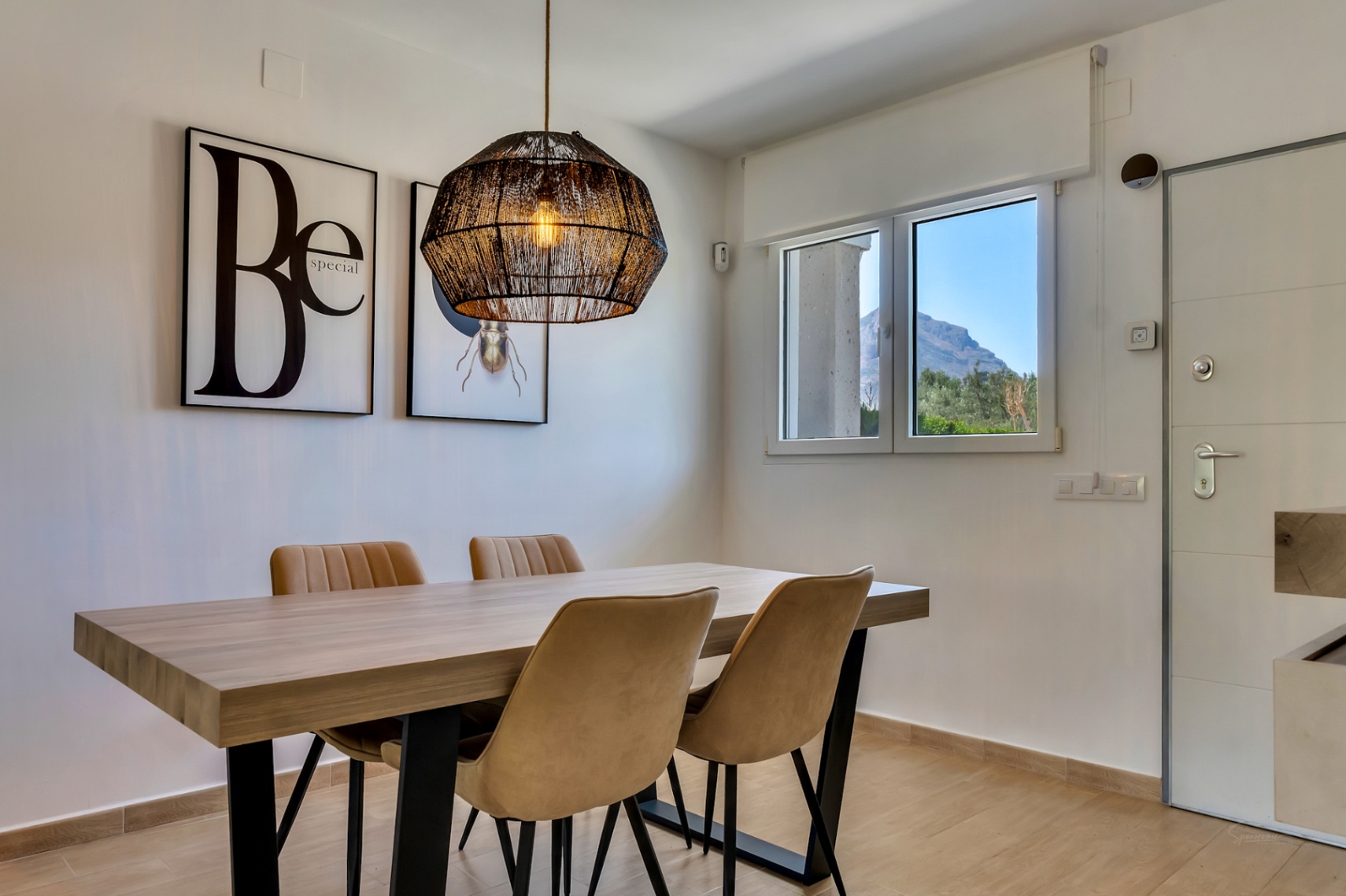Comedor moderno con mesa de madera, sillas tapizadas y lámpara de fibras naturales. La ventana ofrece vistas despejadas a la montaña del Montgó.