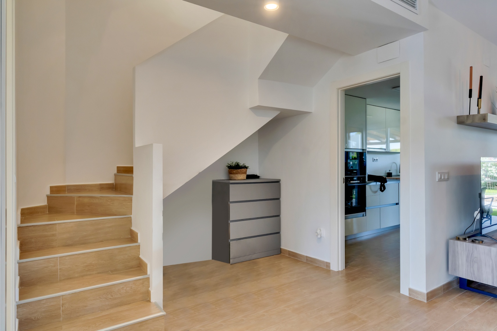 Distribuidor con escalera de gres efecto madera, zona de almacenaje bajo el hueco y acceso directo a la cocina moderna equipada.