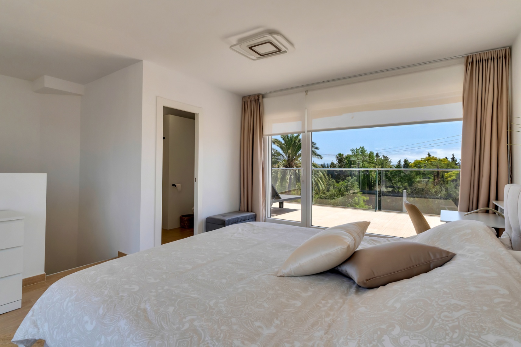 Dormitorio en la planta superior con acceso directo a una terraza privada, ventanales de suelo a techo y baño integrado en suite.