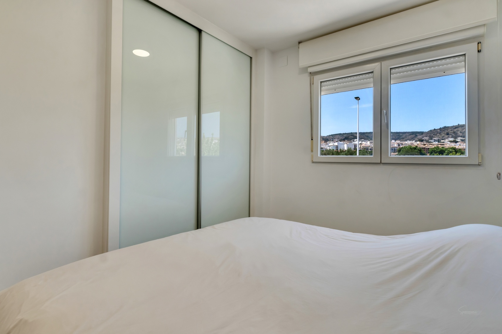Dormitorio luminoso con armario empotrado de puertas correderas en vidrio mate y ventana de climalit con vistas despejadas al entorno de Jávea.