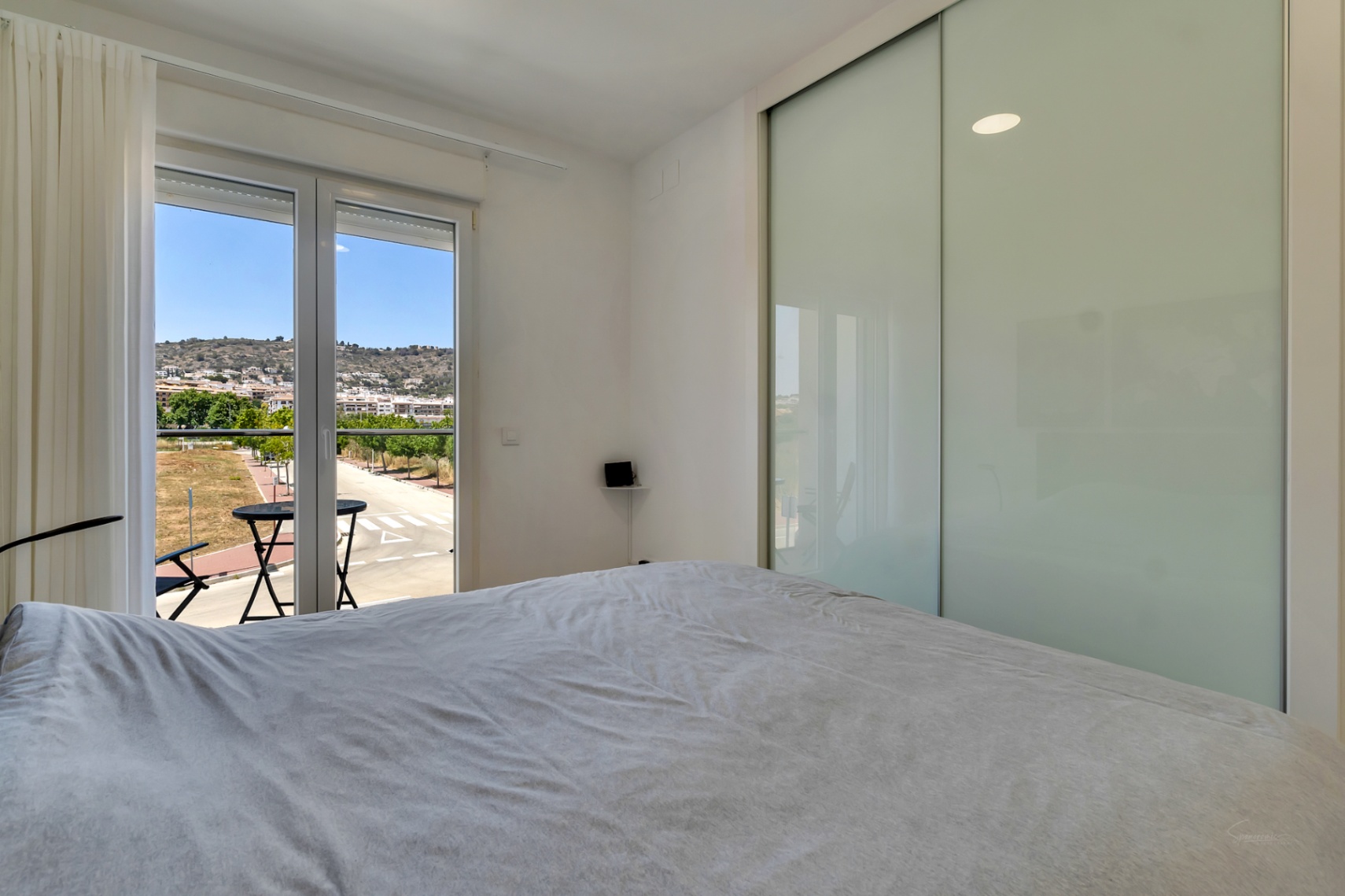 Dormitorio luminoso con armario empotrado de puertas correderas y acceso directo a un balcón privado con vistas despejadas al entorno residencial y las colinas.