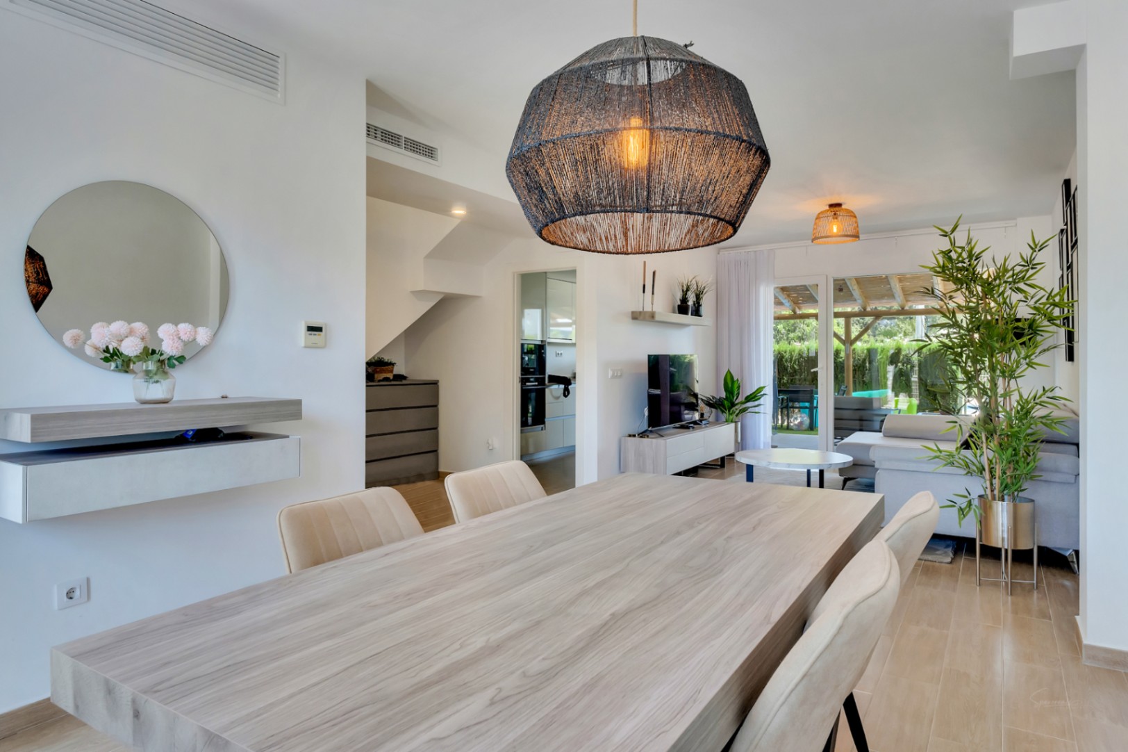 Salón-comedor de concepto abierto con mobiliario de madera clara, lámpara de fibras naturales y acceso directo al patio privado a través de grandes ventanales.