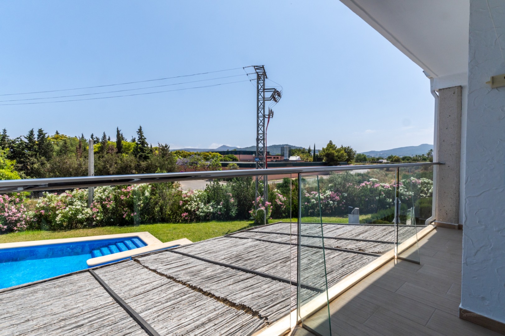 Terraza superior con barandilla de cristal y acero, vistas directas a la piscina comunitaria y al patio privado cubierto con una pérgola de cañizo natural.