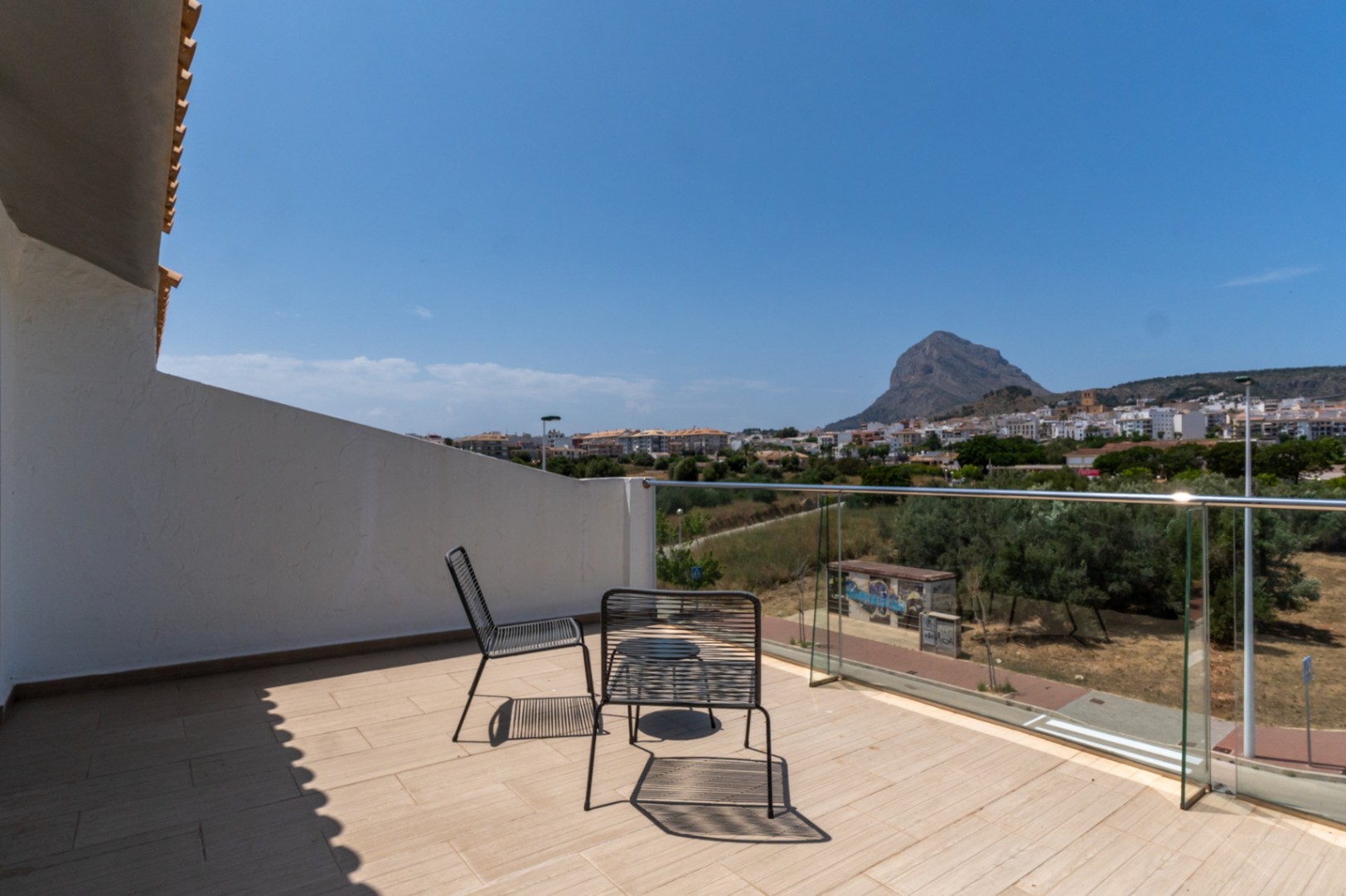 Terraza superior con barandilla de cristal y vistas despejadas al Montgó y al casco antiguo de Jávea. Incluye mobiliario de exterior y suelo cerámico de tonos claros.
